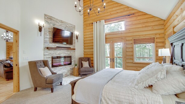 A log cabin bedroom with a large bed, a fireplace, a TV mounted on the wall, and a chandelier. - Hot Tub, Game Room! 3-story Brian Head Home (Brian Head)