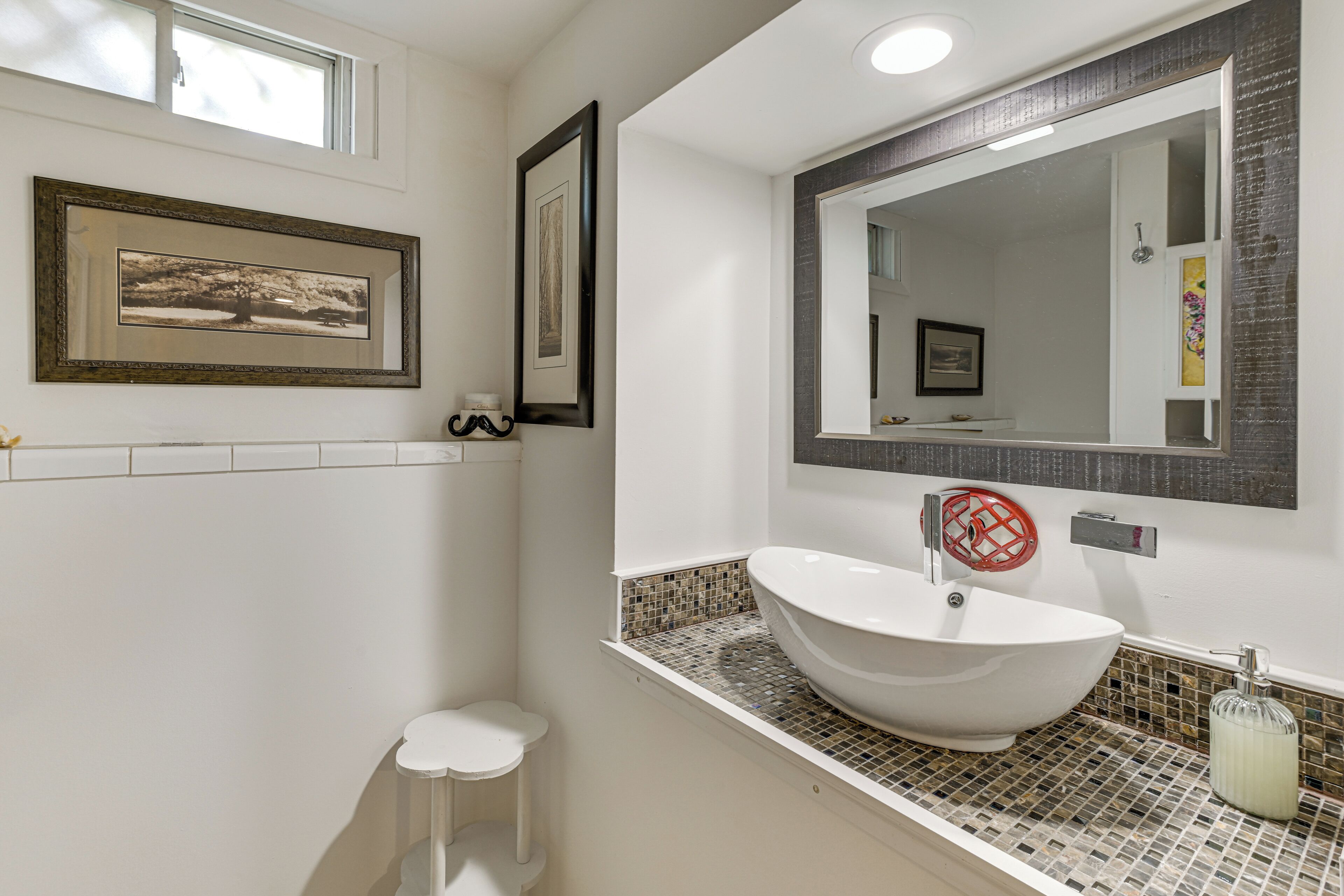 A bathroom with a white sink, a large mirror, and framed pictures on the wall.