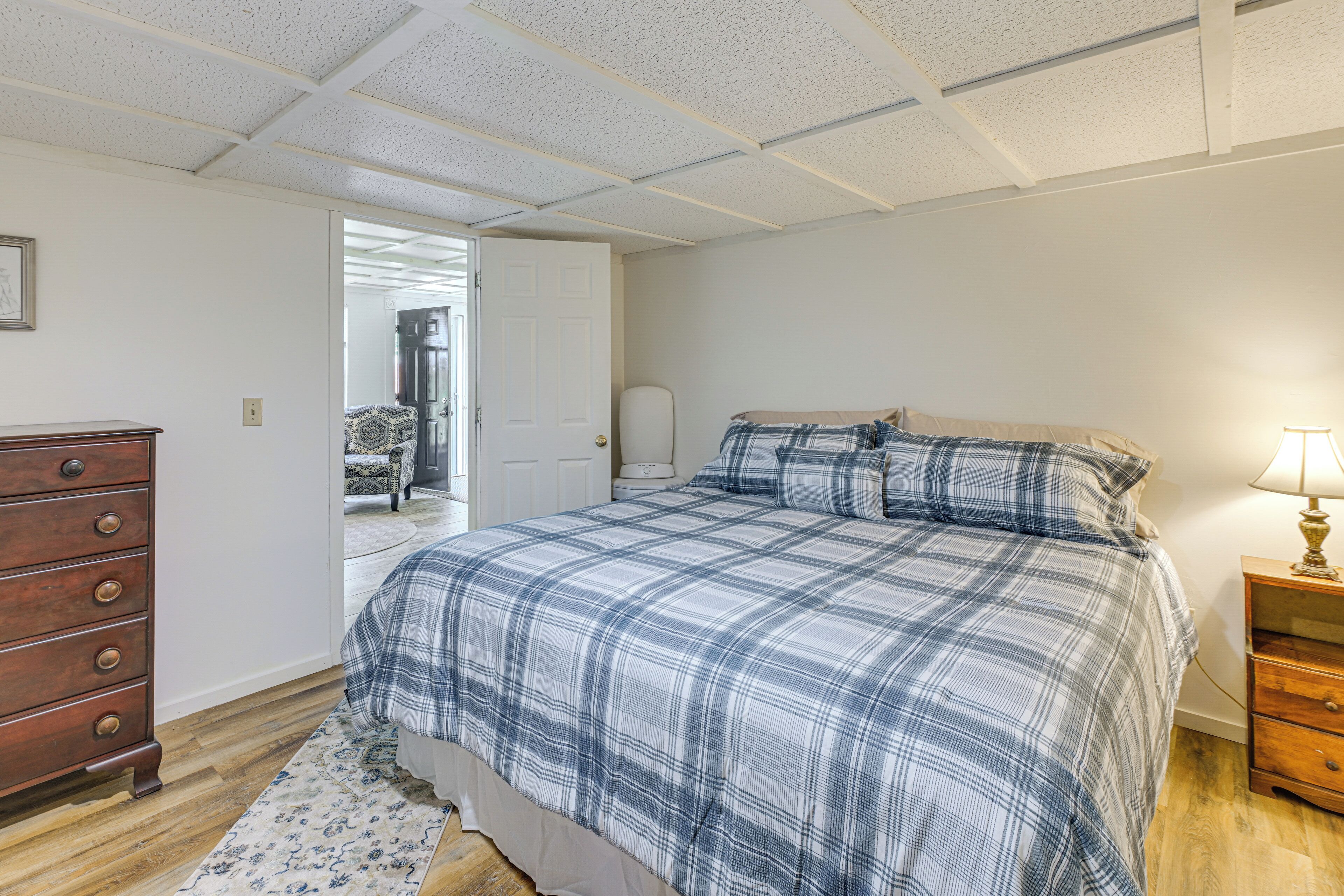 A bedroom with a bed, dresser, nightstand, and a door leading to another room.