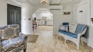 A cozy interior with a patterned armchair, a wicker sofa, and a kitchen area visible through an archway. - Explore Coastal Maine! Cozy Apt w/ Yard & Garden (Orland)
