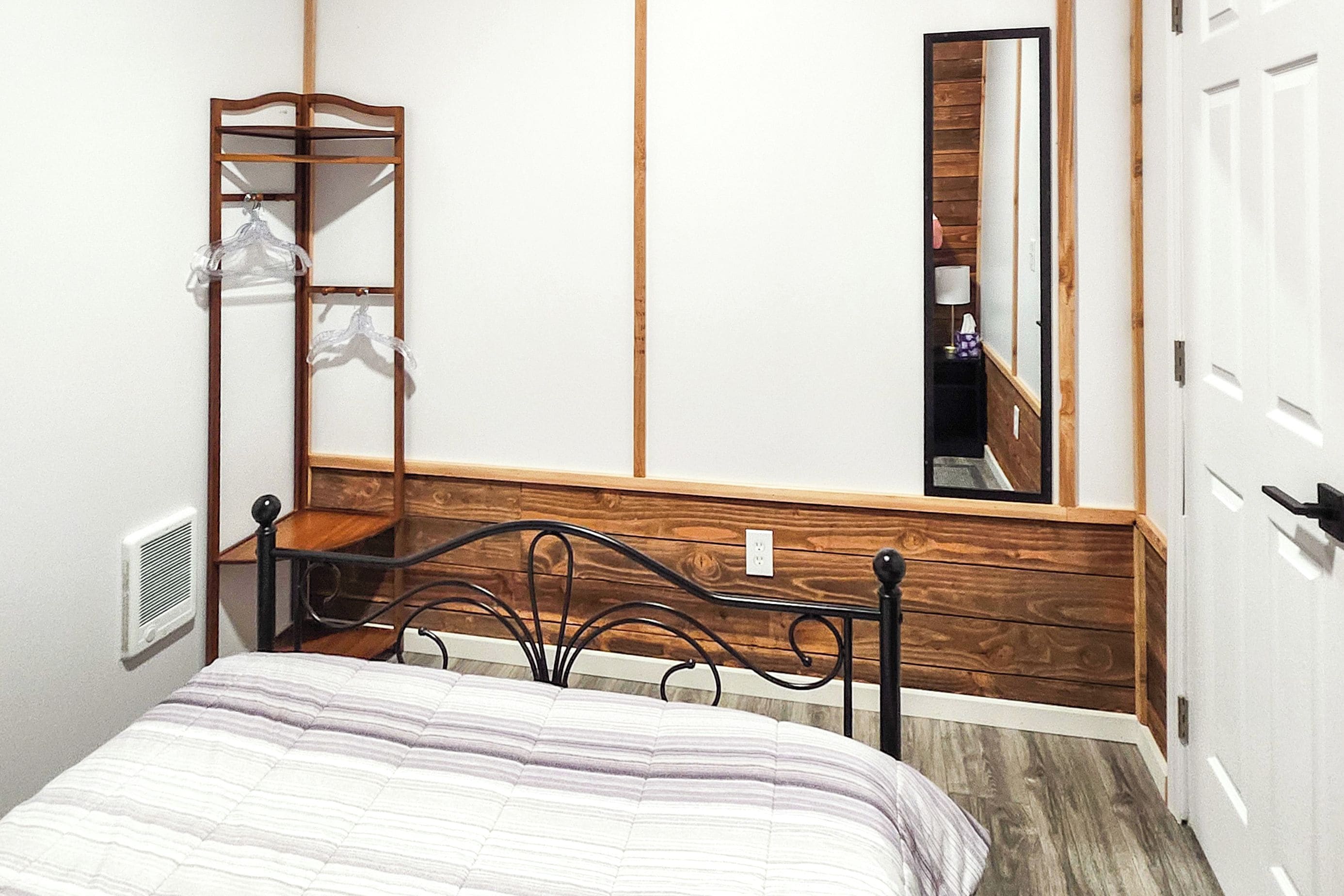 A bedroom with a bed, a wooden headboard, a mirror, and a wardrobe.