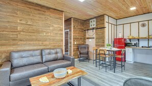 Una sala de estar moderna con un sofá de cuero gris, una mesa de centro de madera y un comedor con una cocina roja al fondo.
