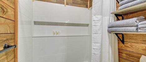 Une salle de bain avec un mur en bois, une baignoire blanche et une étagère avec des serviettes.