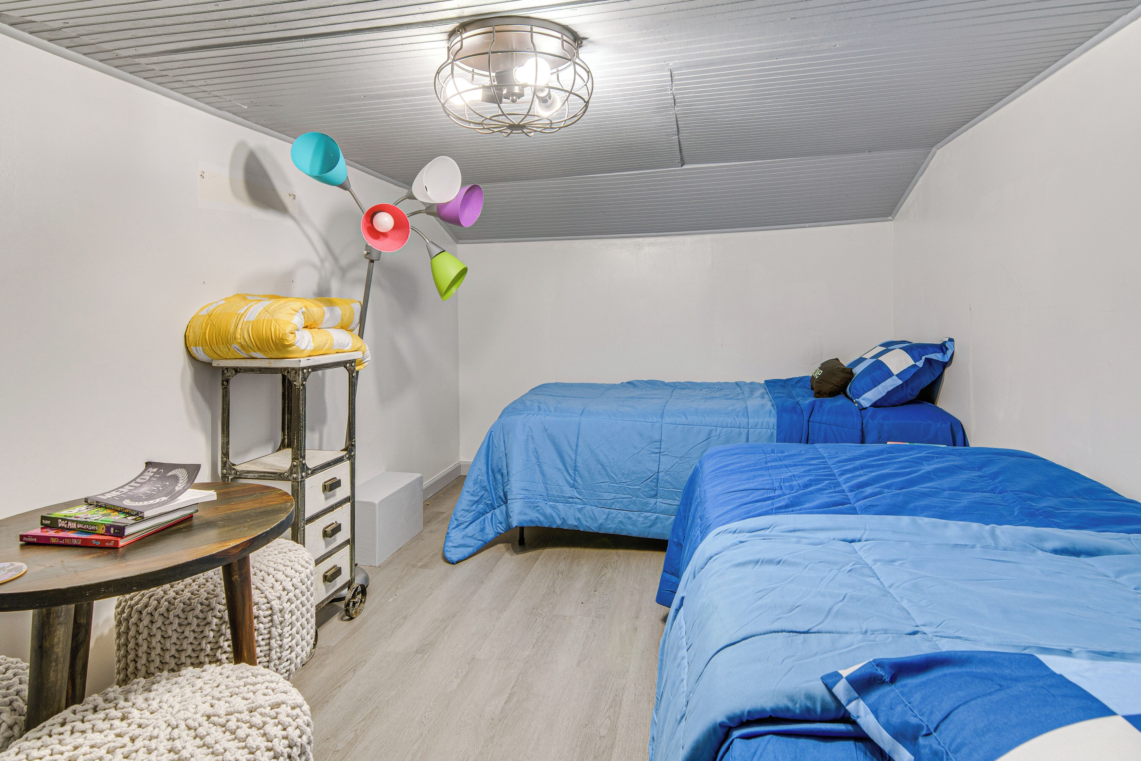 Ein Zimmer mit zwei Betten, einem kleinen Tisch mit Büchern, einer Lampe und einer Deckenleuchte.