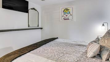 Une chambre à coucher avec un lit, un téléviseur fixé au mur, un tableau encadré et une lampe de chevet.
