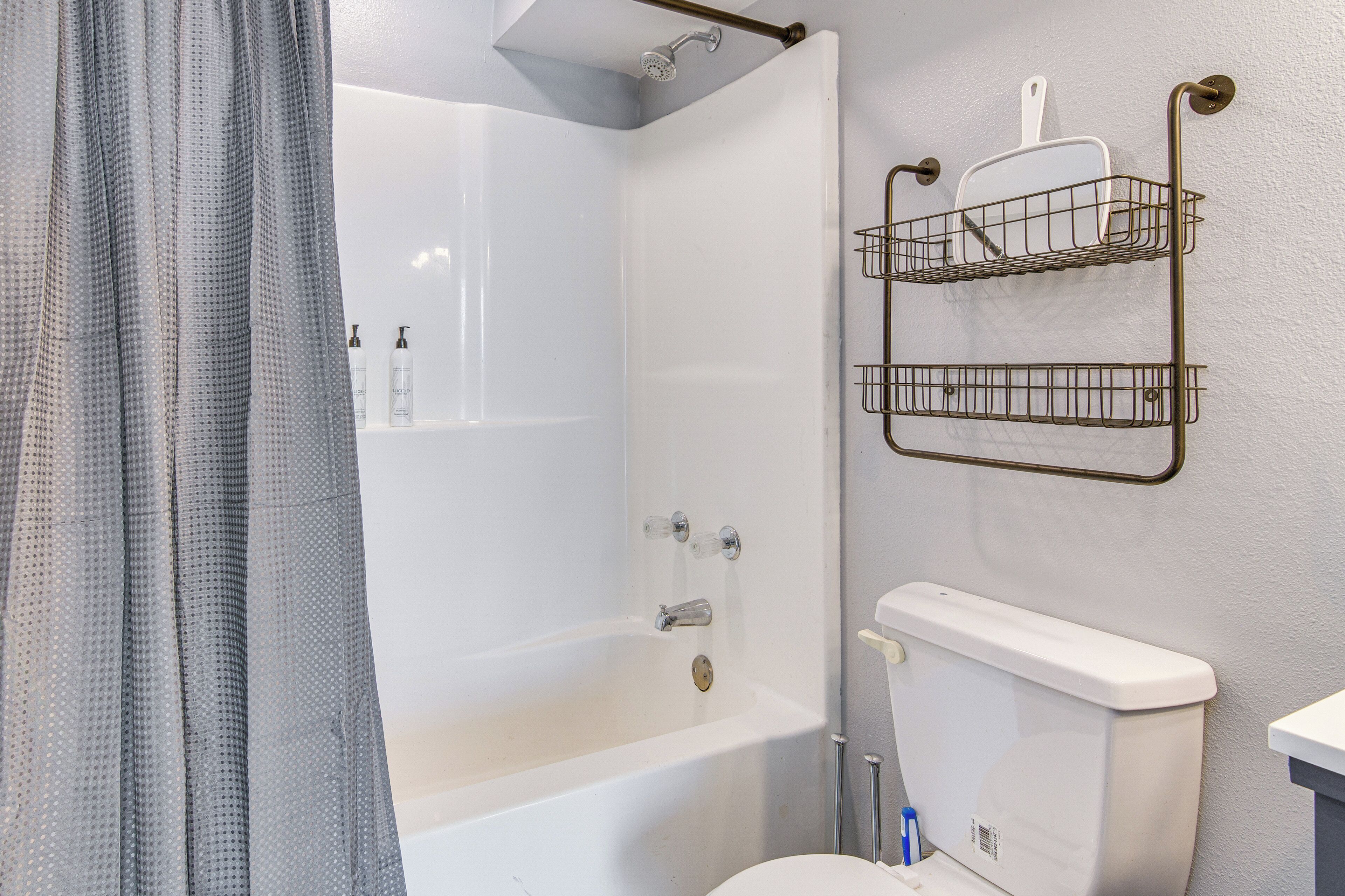Un baño con bañera, inodoro y ducha. Hay dos cestas metálicas fijadas a la pared.