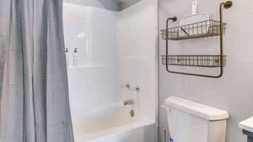 Un baño con bañera, inodoro y ducha. Hay dos cestas metálicas fijadas a la pared.