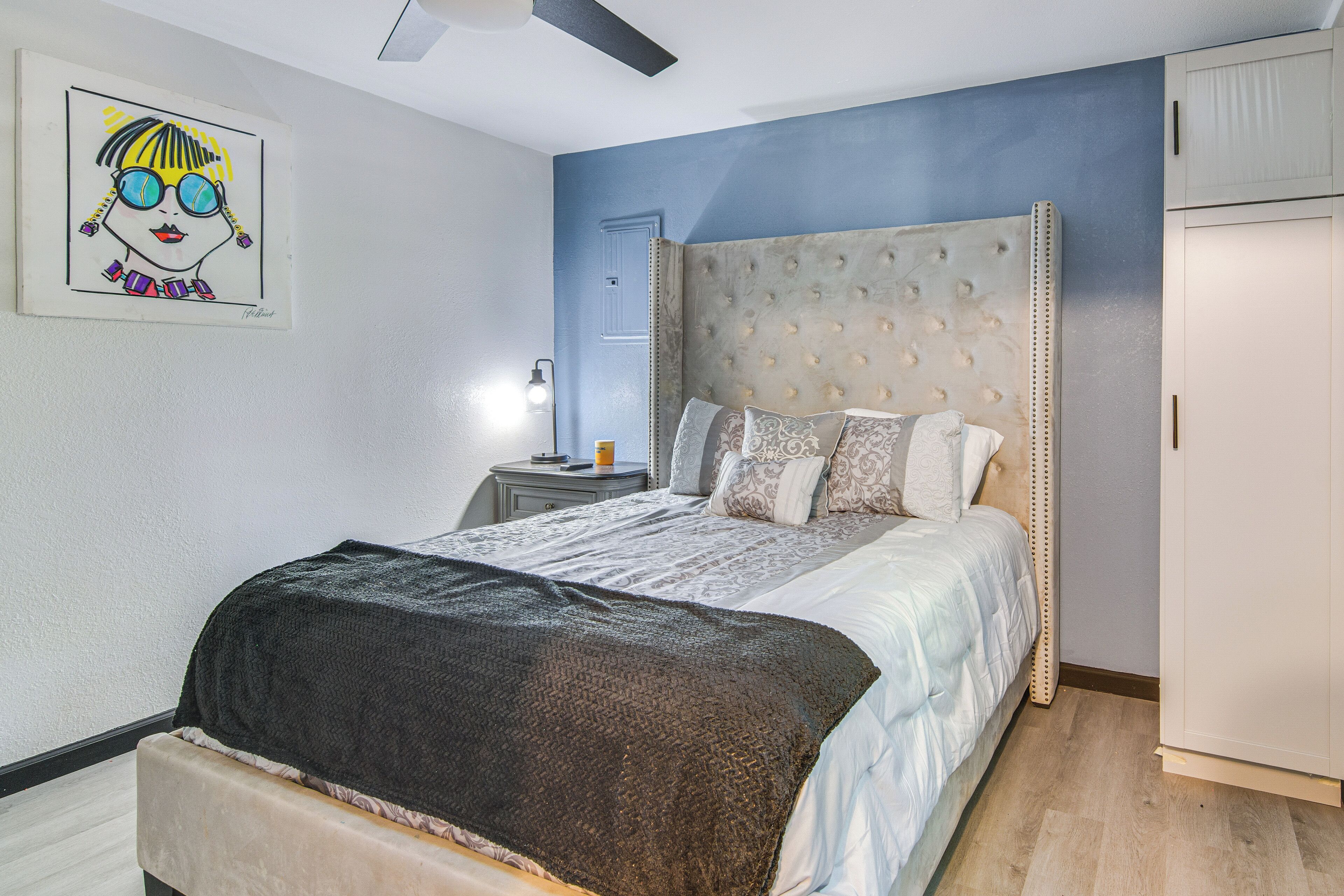 A bedroom with a large bed, a nightstand, a wall-mounted lamp, and a ceiling fan.