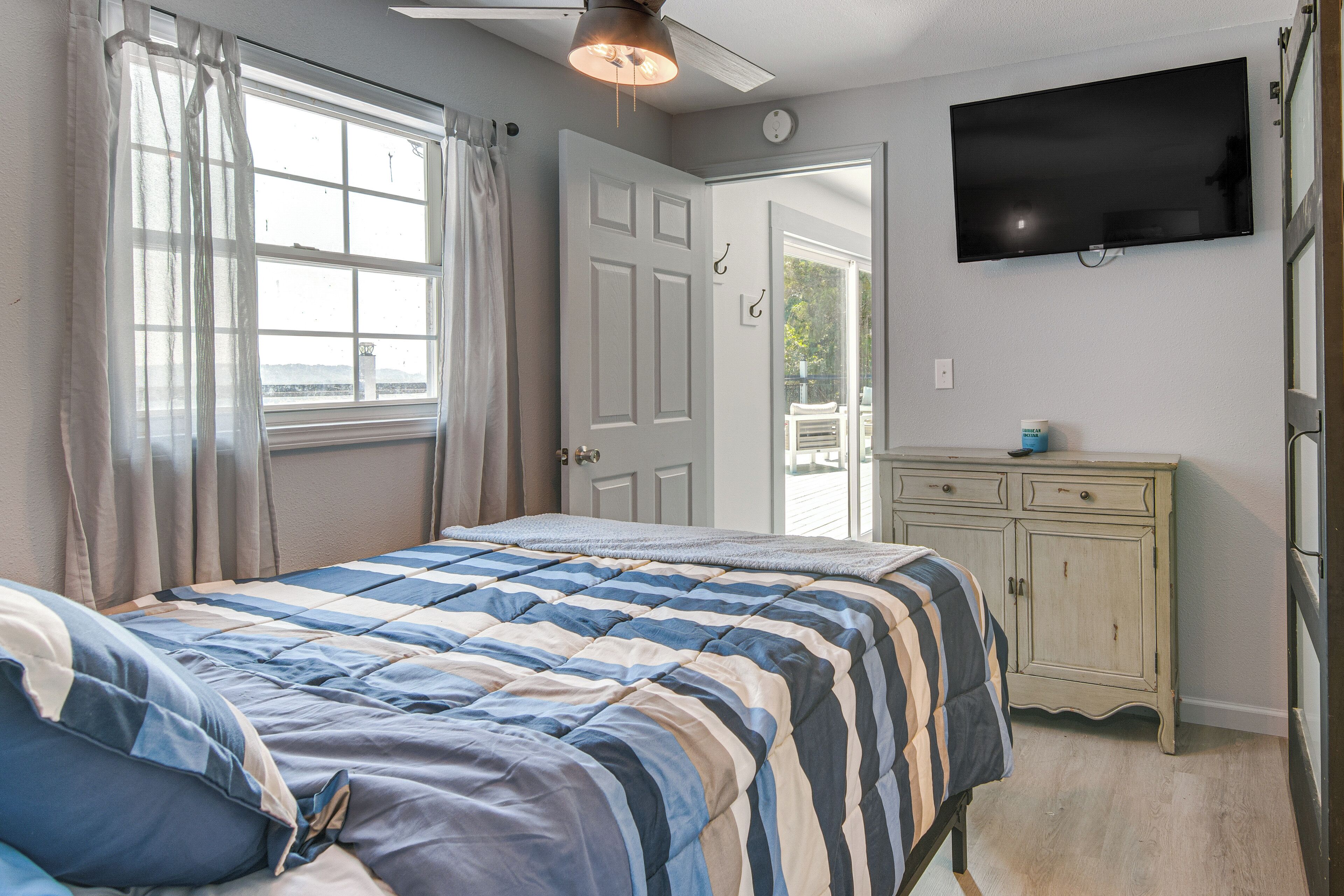 A bedroom with a bed, a television, a dresser, and a door leading to a balcony.