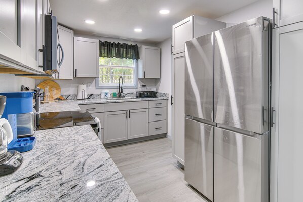 A modern kitchen with white cabinets, a stainless steel refrigerator, and a marble countertop.