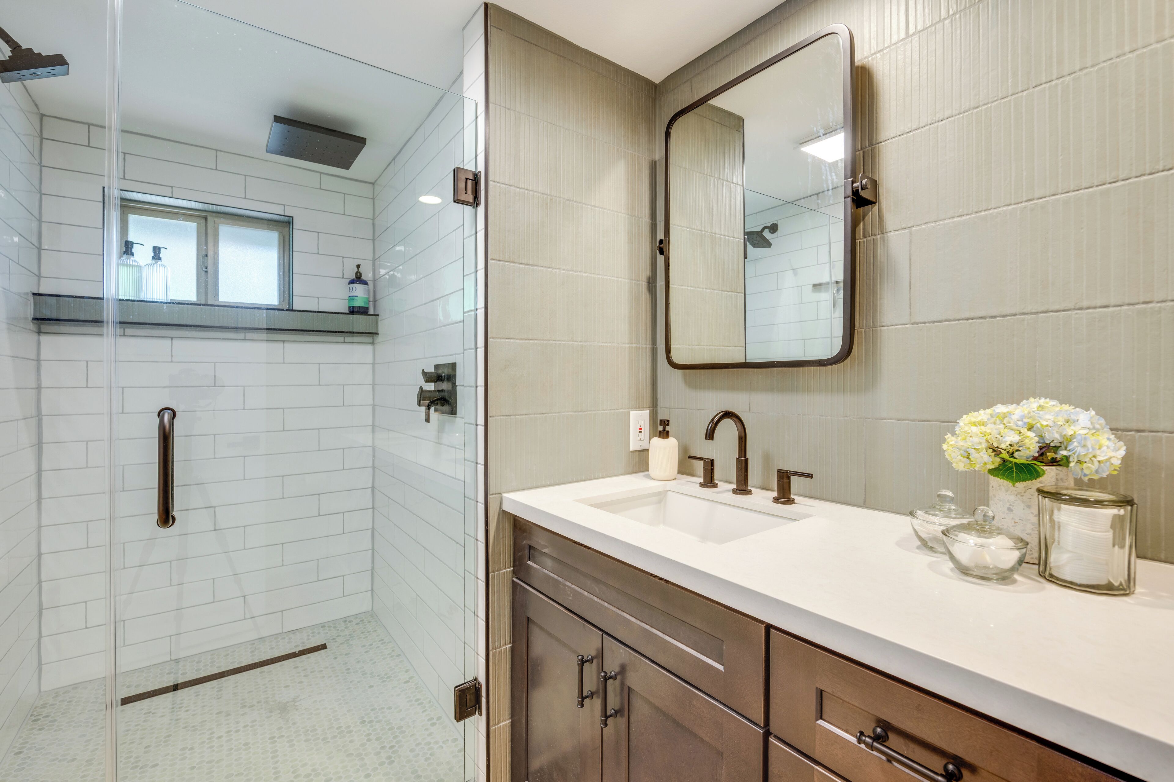 A modern bathroom with a glass shower enclosure, a vanity with a sink, and a mirror.