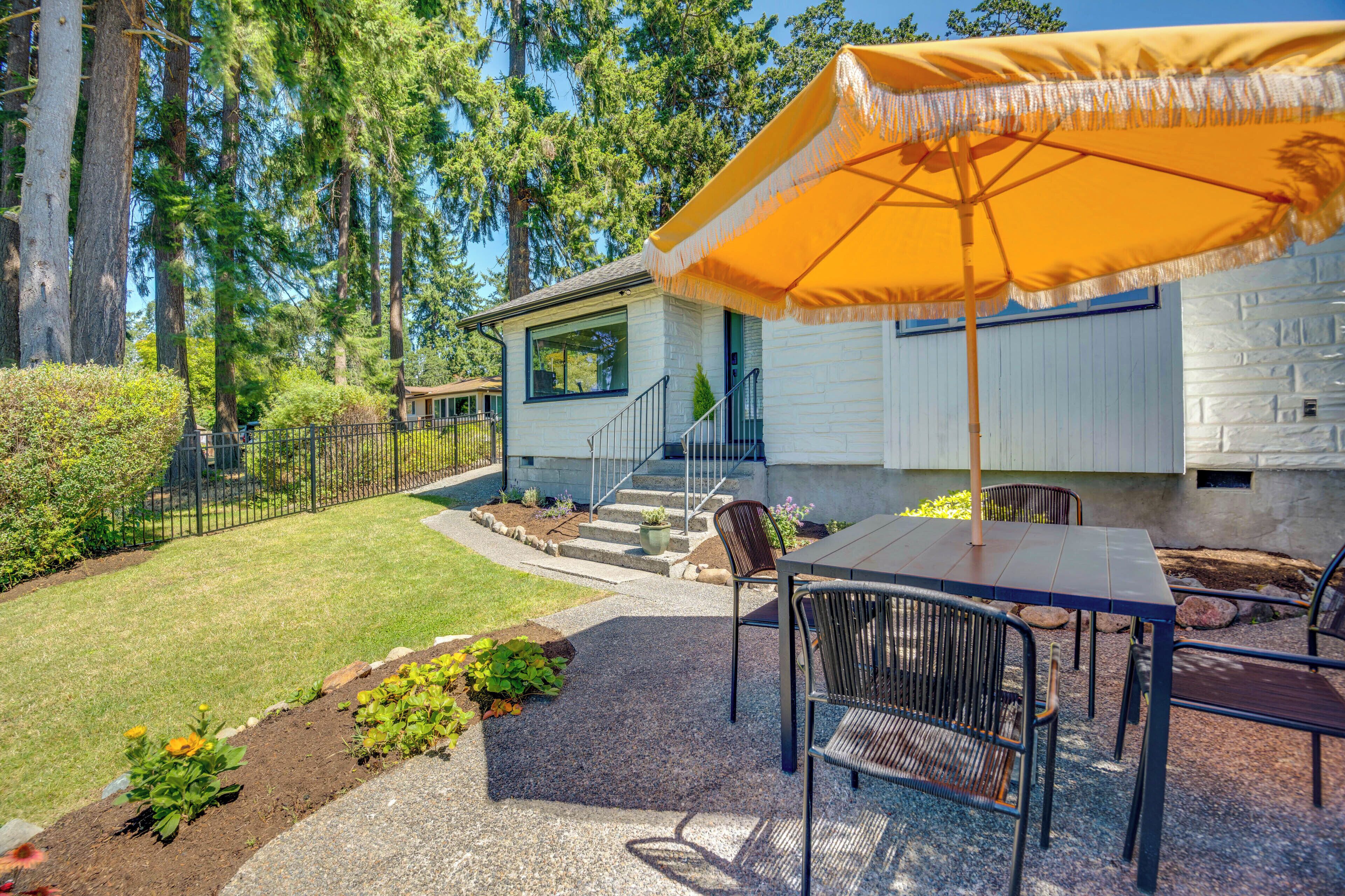 Un espace extérieur aménagé avec une table et des chaises, un parasol, et une maison avec un escalier menant à l’entrée.