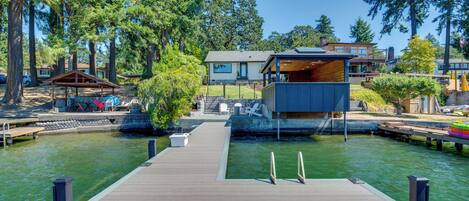 A wooden dock leading to a house with a deck and a small pool.