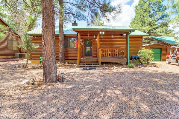 A rustic log cabin with a porch, a front door, and a small front yard with gravel and a tree.