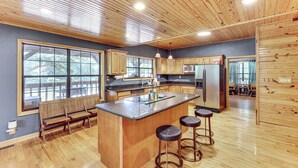 Une cuisine spacieuse avec des meubles en bois, un grand îlot central doté de tabourets et une vue agréable par les fenêtres.