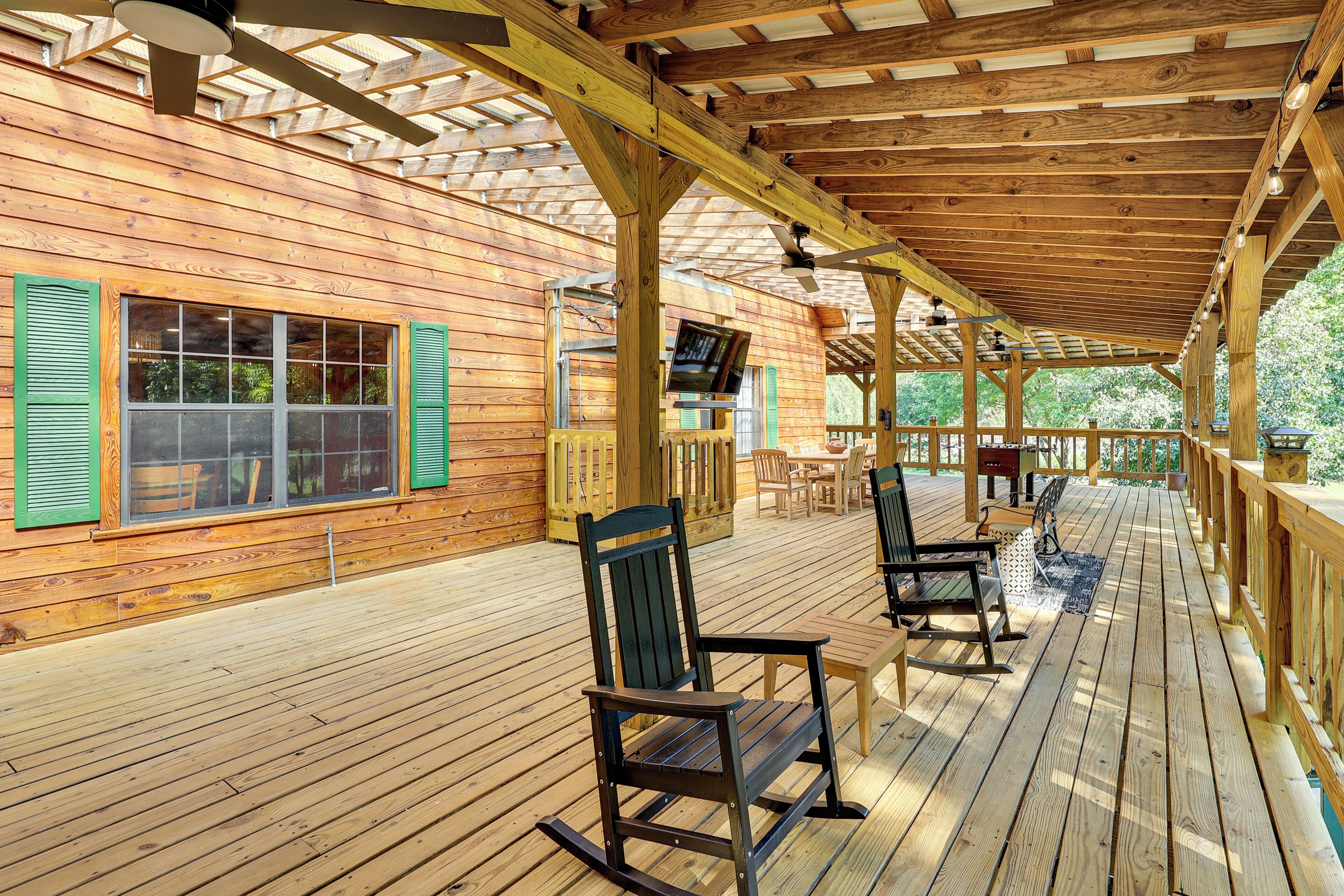 Una terraza cubierta de madera con mecedoras, un televisor y una mesa.
