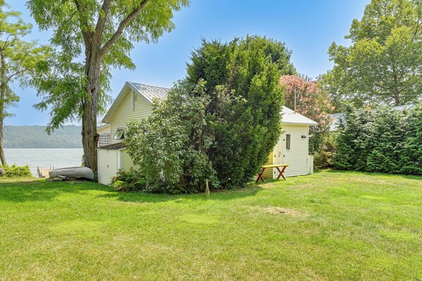 A lakeside cabin with a grassy yard, a dock, and a boat. - Dock & Rowboat: 'beechnut Bungalow' on Keuka Lake (Branchport)