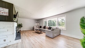 A spacious living room with a fireplace, a large window, and a modern sofa set. - Home < 1 Mi to Lake Erie & Shades Beach Park! (Harborcreek)