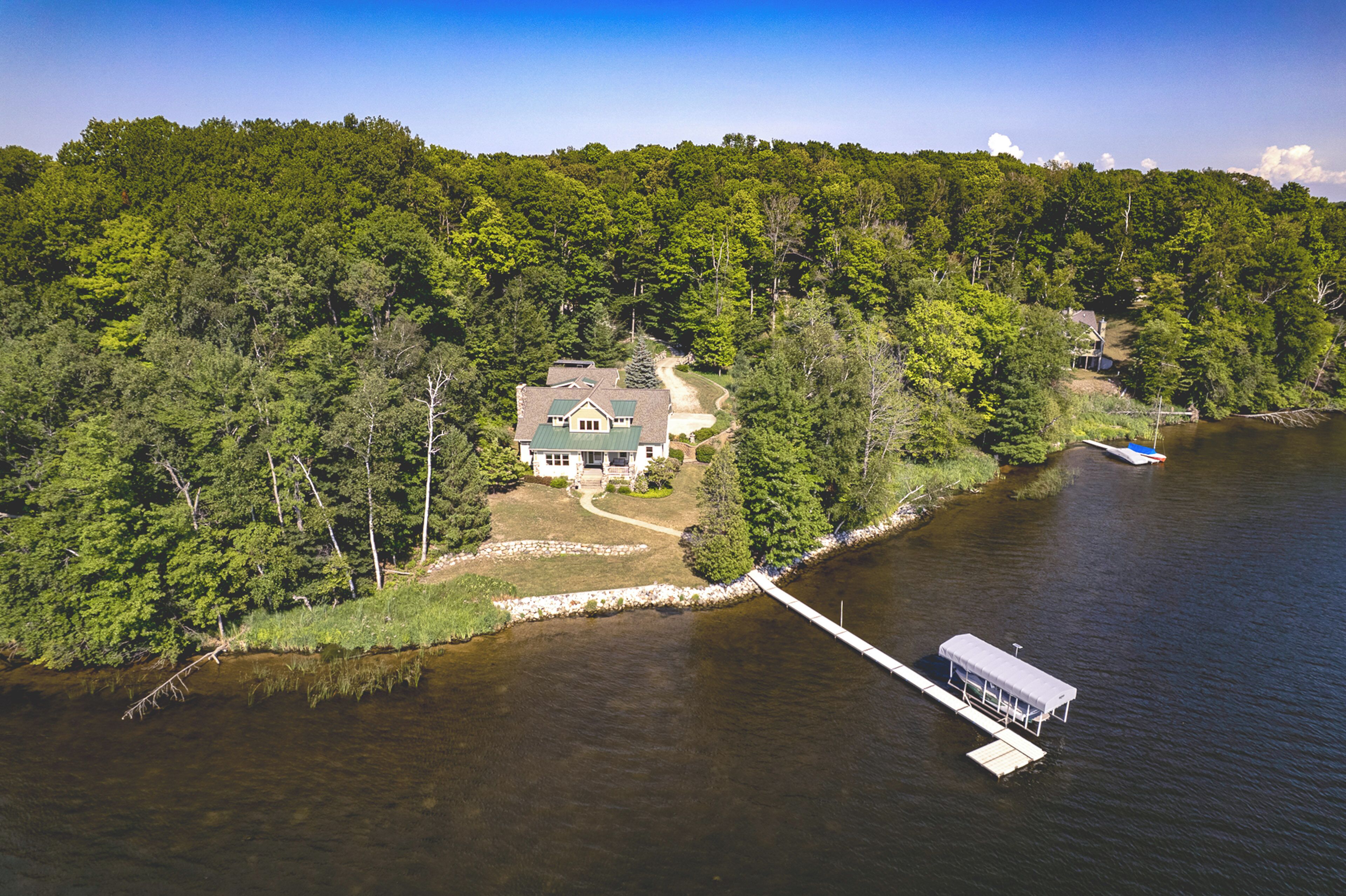 Una casa a orillas del lago con un muelle que se adentra en el agua, rodeada de un bosque frondoso.