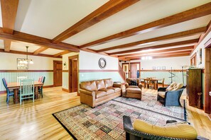 Un salón amplio con vigas de madera, un sofá de cuero marrón, un tapete estampado y un comedor con mesa y sillas de madera.