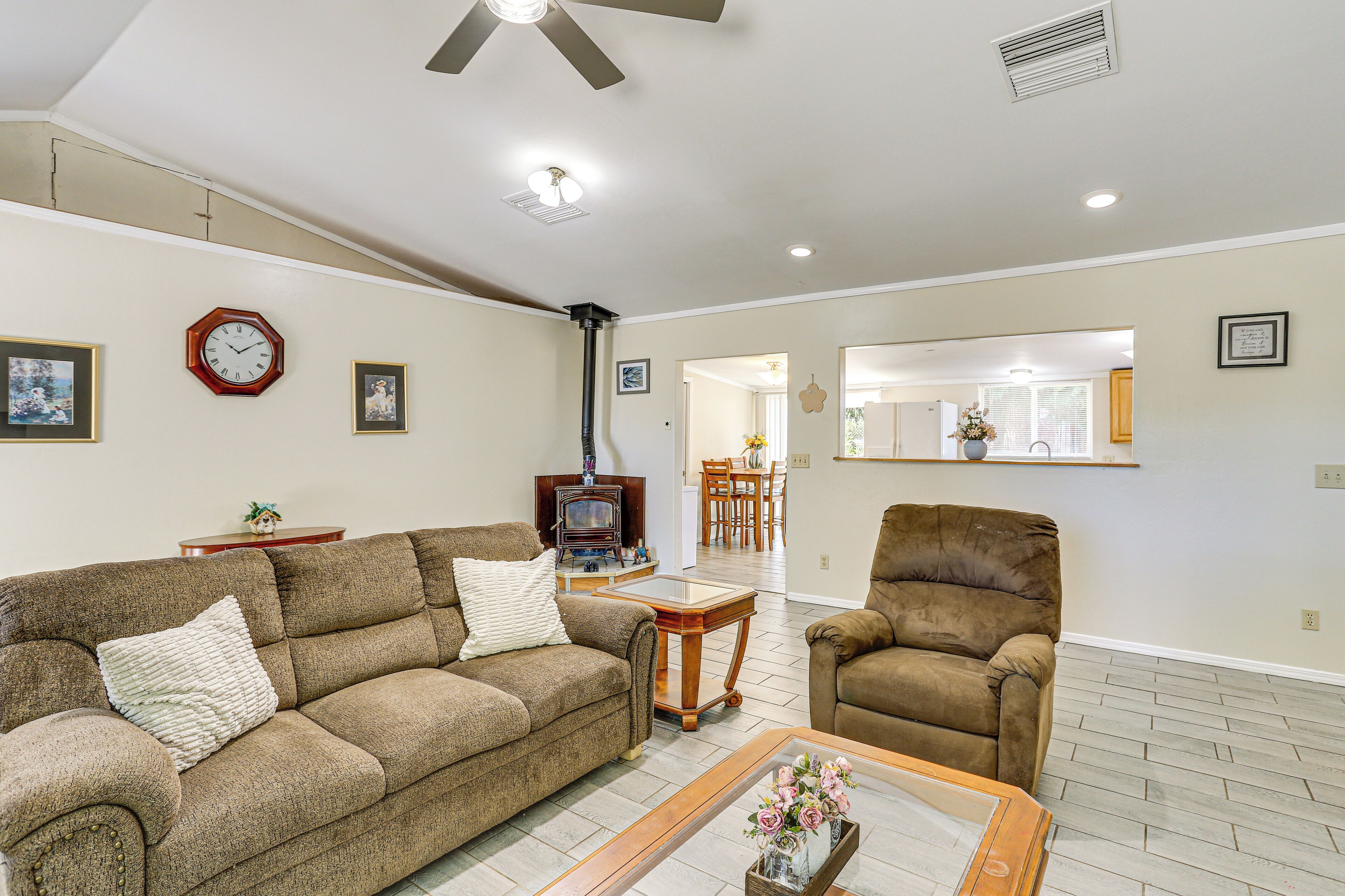 A living room with a brown sofa, a brown armchair, a coffee table with a vase, and a clock on the wall.