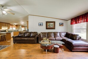 A spacious living area with a brown leather sectional sofa, a glass coffee table, and a dining area with wooden cabinets and a kitchen in the background. - Play Games, Bike & Unwind: Cleveland Family Home! (Cleveland)