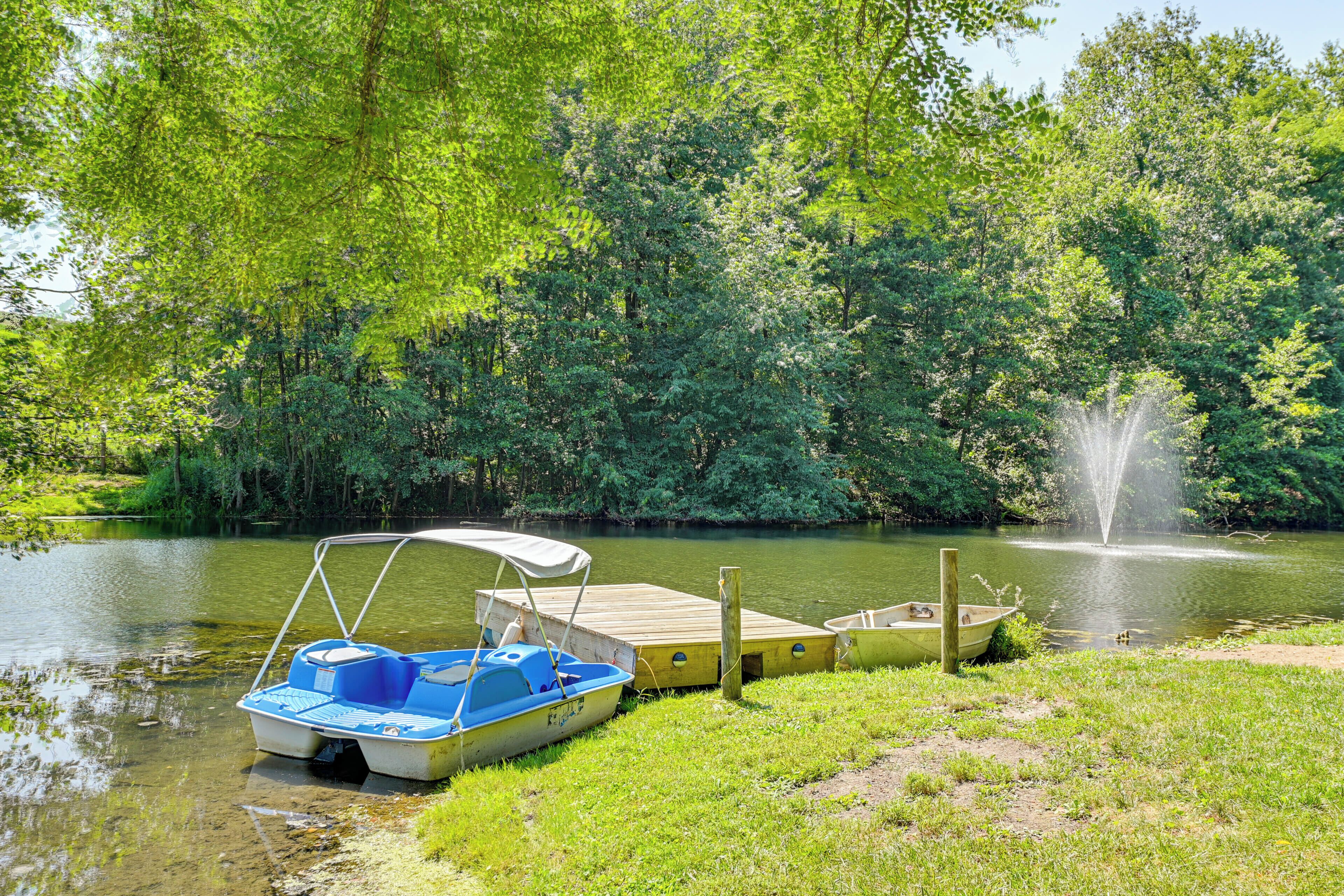A tranquil lakeside scene with a dock, a small boat, and a fountain.