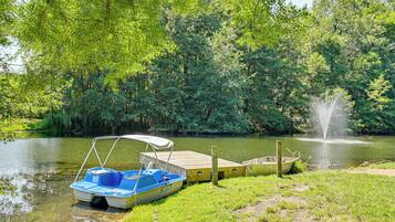 A tranquil lakeside scene with a dock, a small boat, and a fountain.