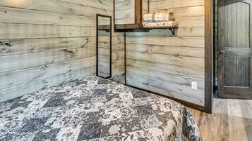 A room with wooden walls, a bed with a patterned bedspread, a mirror, and a shelf with a blanket.