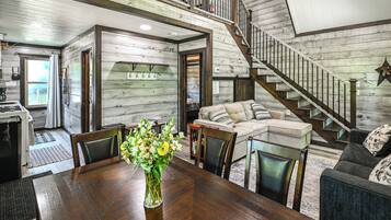 A spacious living area with a wooden staircase, a dining table with chairs, and a sofa.