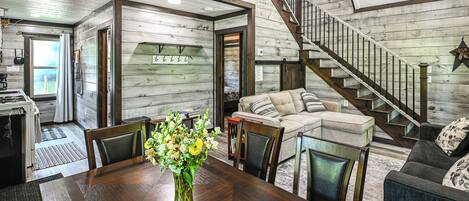 A spacious living area with a wooden staircase, a dining table with chairs, and a sofa.