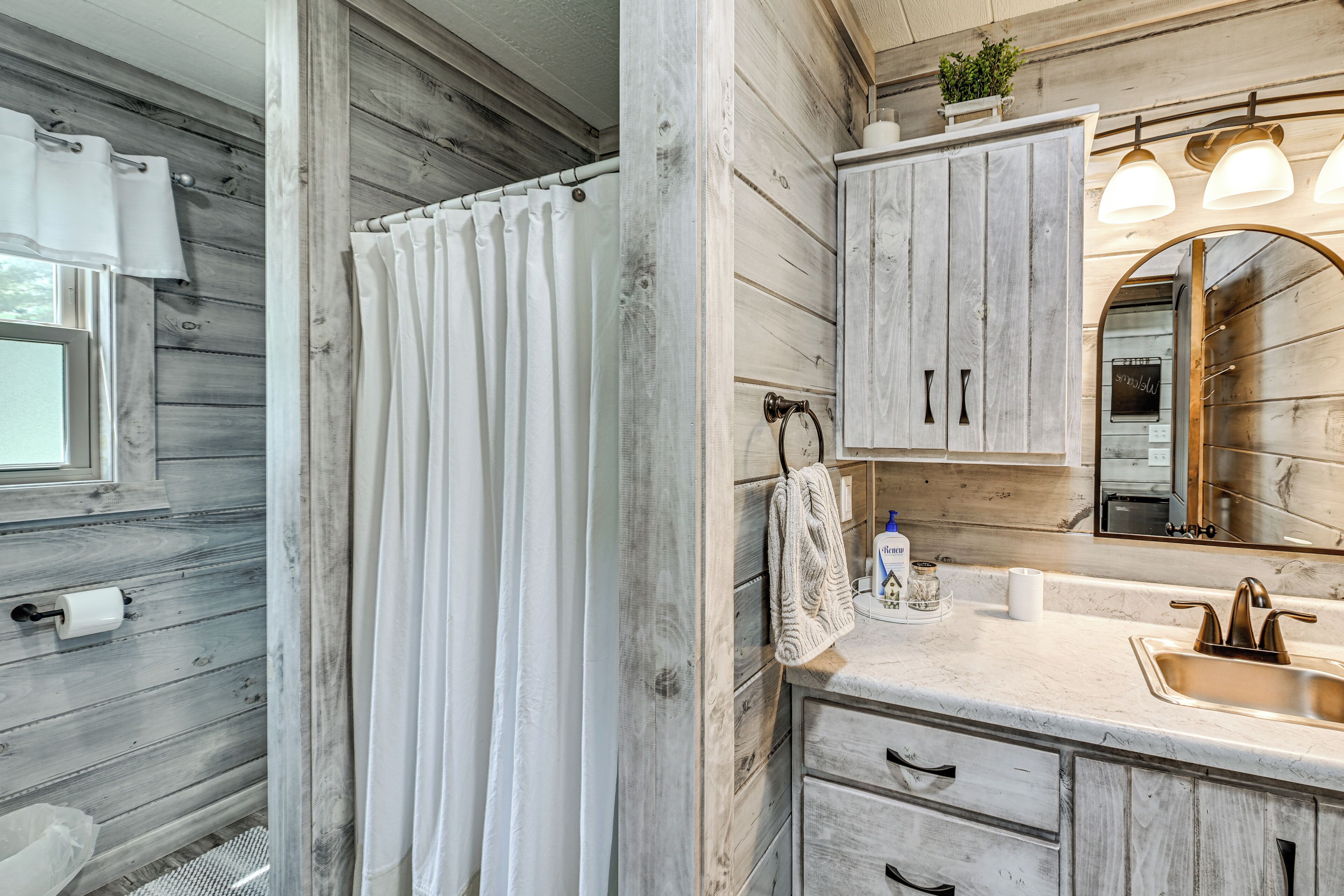 A bathroom with wooden walls, a shower curtain, a sink with a gold faucet, and a mirror with lights above it.