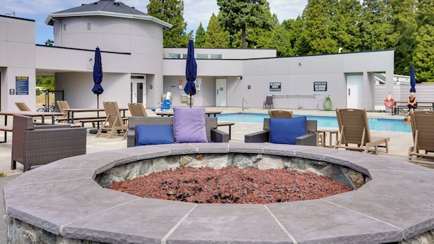 A poolside area with lounge chairs, a fire pit, and a building with a pool. - 1 Mi to Birch Bay SP! Cozy Cabin w/ Pool Access (Blaine)
