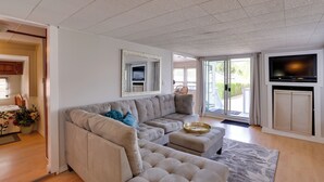 A living room with a sectional sofa, a flat-screen TV, and a sliding glass door leading to an outdoor area. - 1 Mi to Birch Bay SP! Cozy Cabin w/ Pool Access (Blaine)