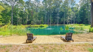 A serene lakeside setting with two wooden benches facing a calm green lake, surrounded by dense forest. - 1/2 Acre Pond, Rec Room! Private Oasis in Nanjemoy (Nanjemoy)
