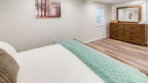 A bedroom with a bed, a dresser, a mirror, and a painting on the wall.