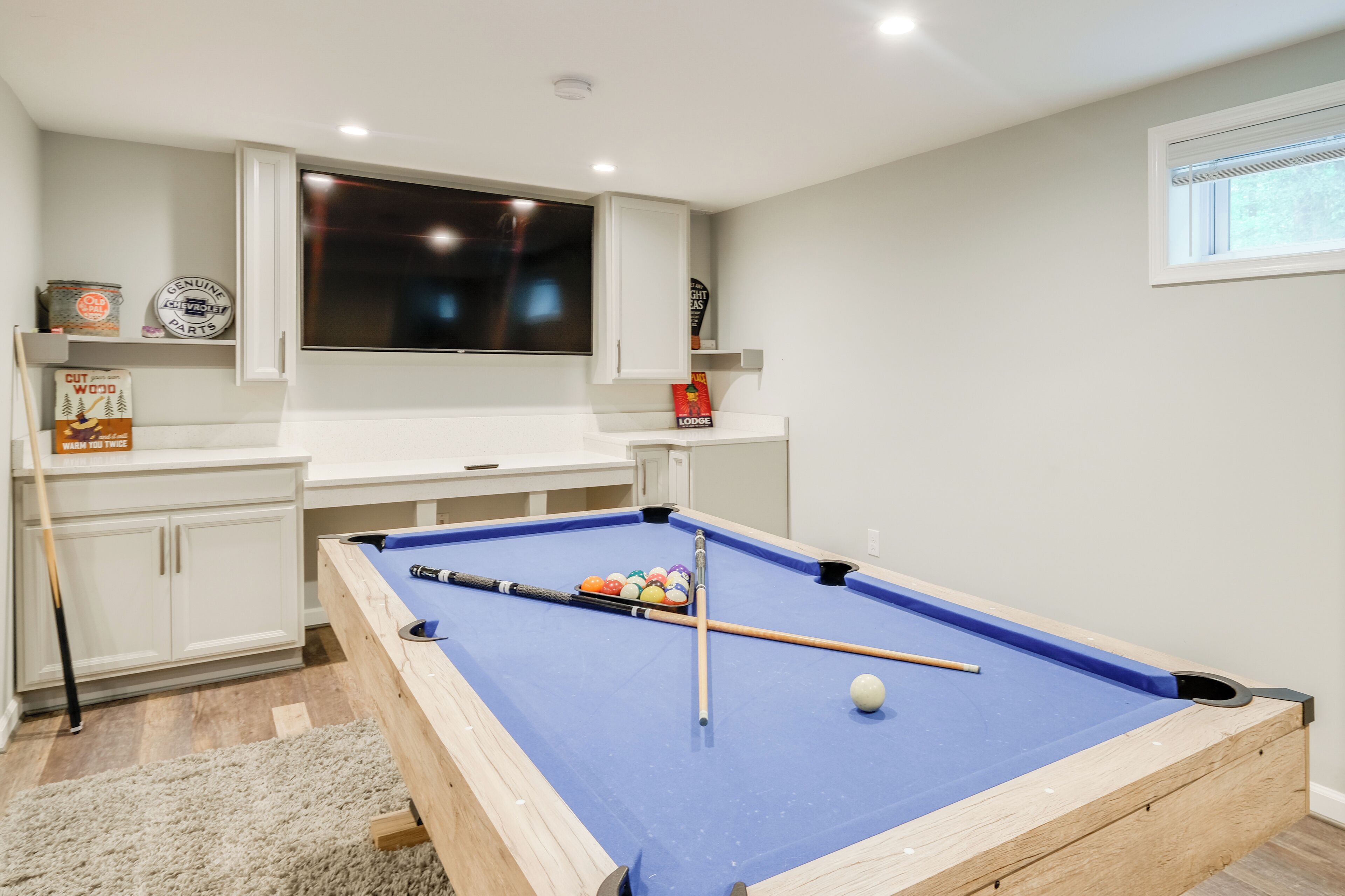 A pool table in a room with white cabinets and a mounted television.