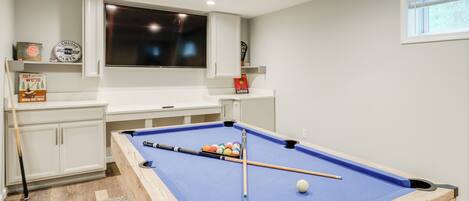 A pool table in a room with white cabinets and a mounted television.
