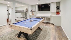 A pool table in a room with a bunk bed, a TV, and a shelf with items.