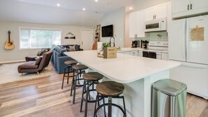 A modern kitchen with white cabinets, a large island with stools, a guitar, and a cozy seating area with a sofa and cushions.