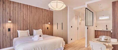 Een moderne hotelkamer met een houten accentmuur, een groot bed, een zithoek met een tafel en stoelen, en een trap naar een ander niveau.