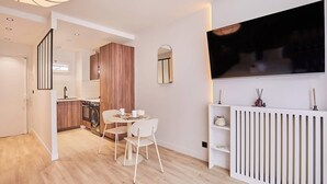 Una cocina moderna con armarios de madera, un comedor con dos sillas y un televisor en la pared.