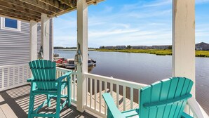 Une terrasse couverte avec deux fauteuils Adirondack turquoise, une vue sur un lac paisible et, au loin, une côte bordée de bâtiments.