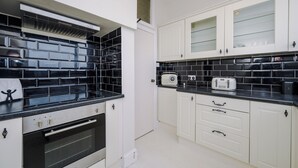 A kitchen with black and white tiles, a built-in oven, and white cabinets with glass doors. - Pier View House - Blackpool (Blackpool)