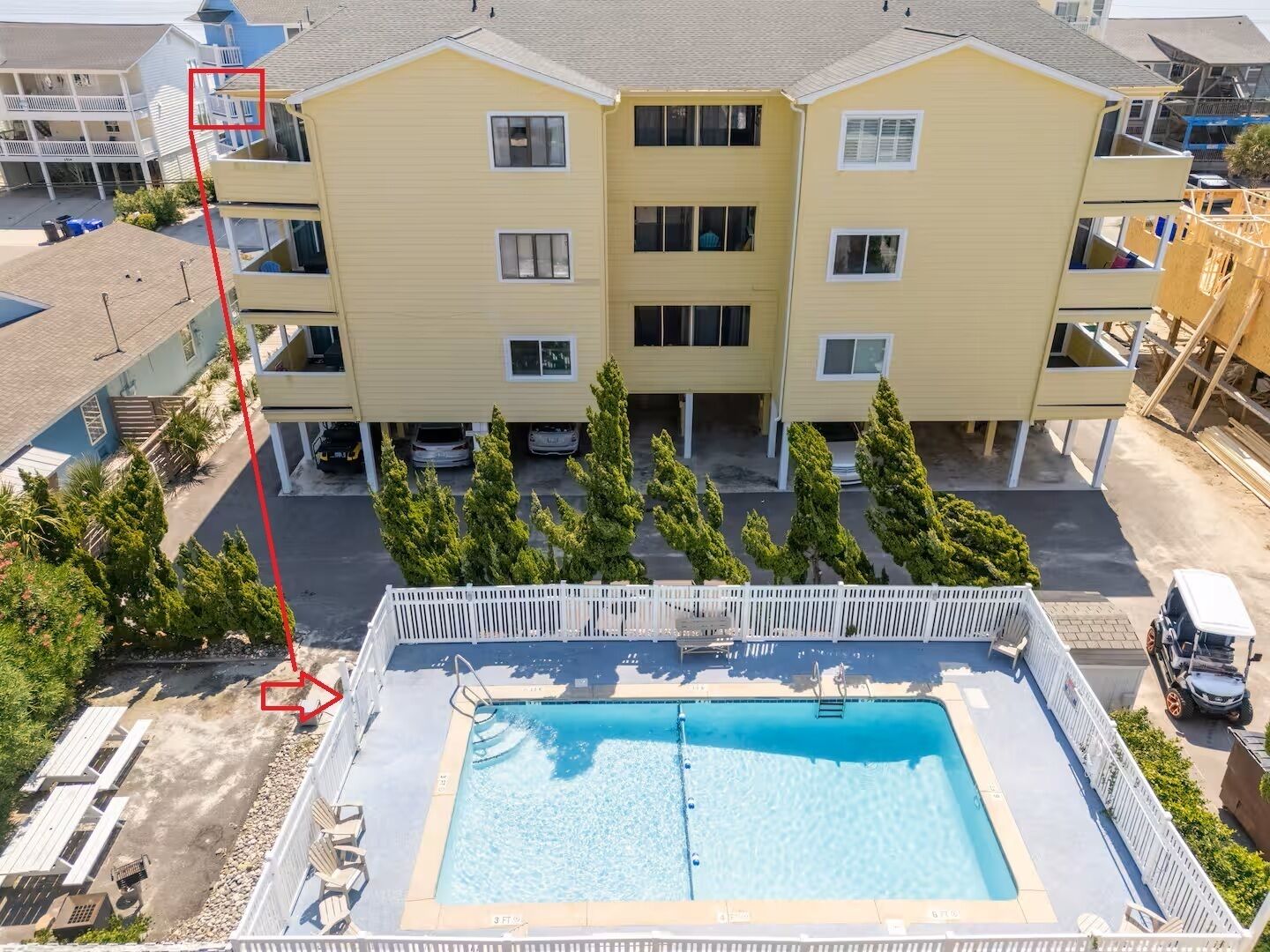 Un immeuble jaune à plusieurs étages, avec une piscine devant.