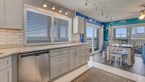 A modern kitchen with a dishwasher, white cabinets, and a blue accent wall. - Sunskipper Panoramic Ocean Front - 2br oceanfront condo in Carolina Beach (Carolina Beach)