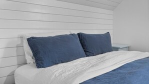 Ein ordentlich bezogenes Bett mit weißer und blauer Bettwäsche, ein weißer Kopfteil und ein Nachttisch mit einer Lampe.
