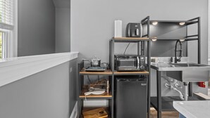 Een compacte keuken met een inbouwmagnetron, broodrooster en spoelbak, uitgevoerd in een modern design met grijze wanden en houten planken.