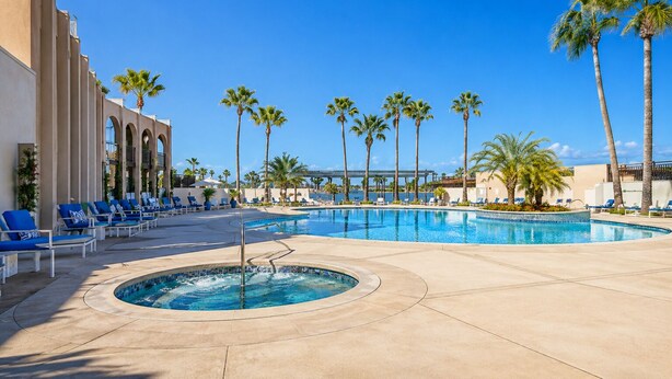 A pool area with lounge chairs, palm trees, and a clear sky.