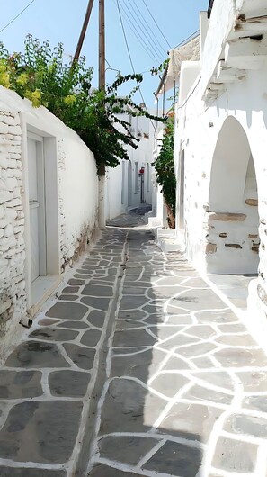 A narrow, stone-paved alleyway flanked by white buildings with arched doorways and windows.